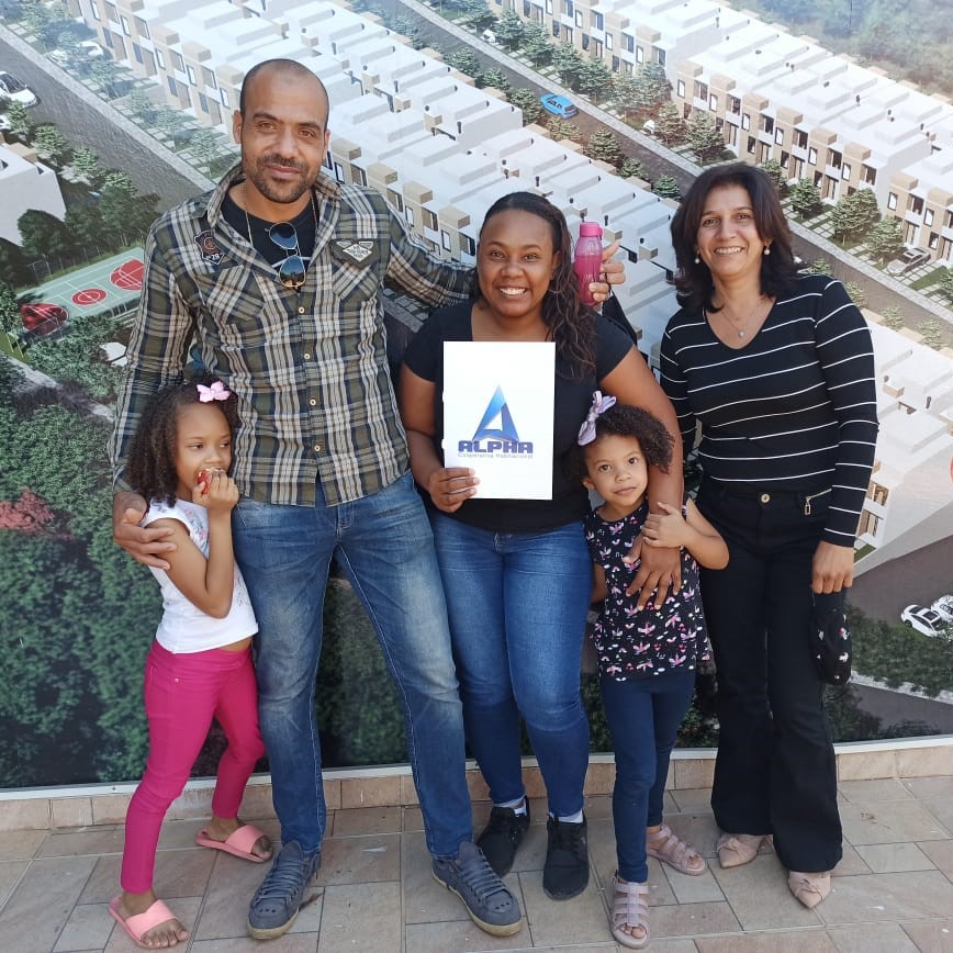 cooperada Adriana, seu marido e suas duas filhas segurando o plano da alpha cooperativa ao lado da corretora Silmara