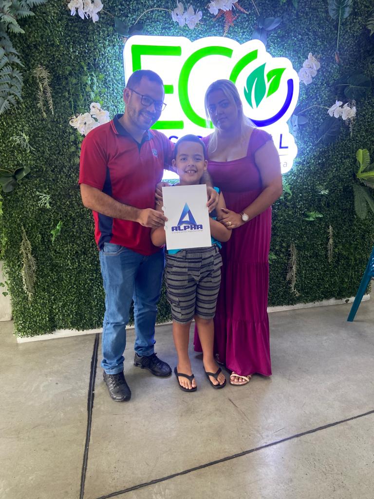 Filha da cooperada 10 segurando o plano da Alpha Cooperativa ao lado de seus pais e sua avó